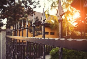 Exquisite wrought iron fence guarding a property with the sun aligning the horizon behind silhouette of trees and leaves. 