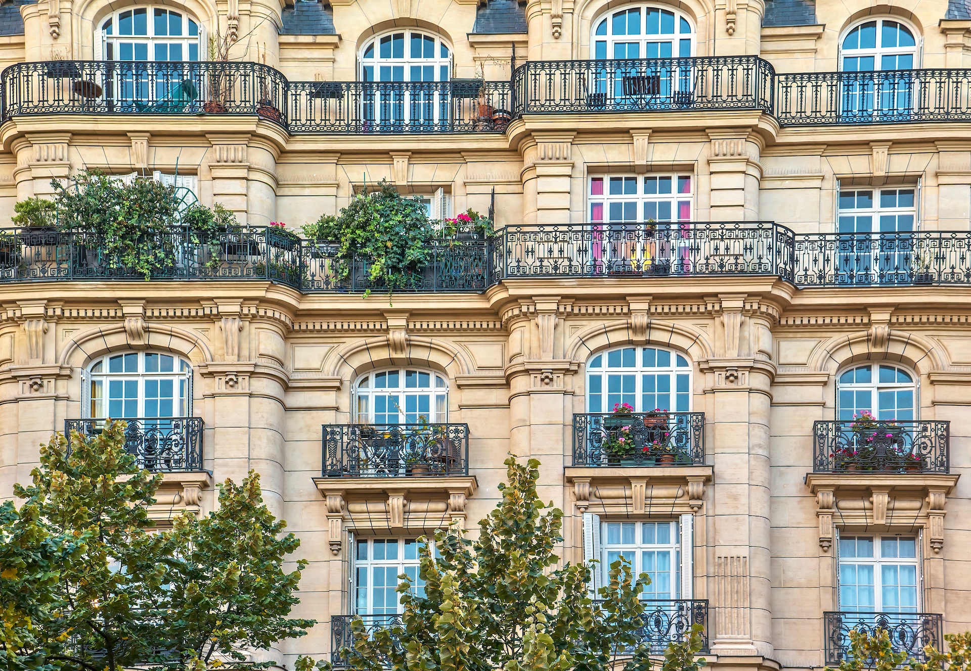 Street view of an old, elegant residential building facade in Paris, with ornate details in the stone walls, french doors and wrought iron railings on the balconies.